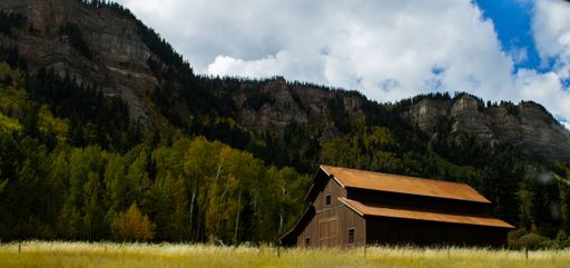 A beautiful view of an old house in a field and mountains with trees on a sunny day