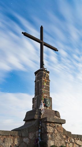 A vertical shot of metal cross on Matagalls peak on blue cloudy sky background in Montseny Massif