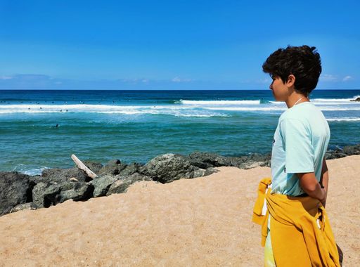 A young Hispanic boy looking at surfers from a seashore