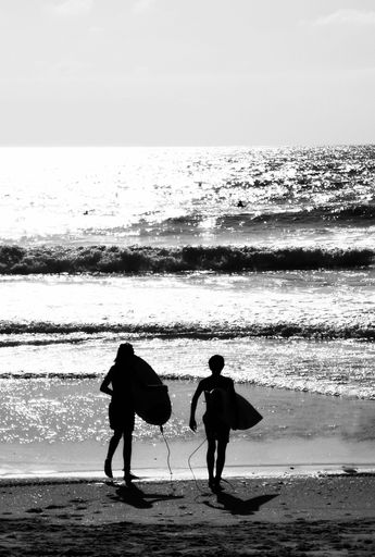 A vertical grayscale shot of a couple with surfboards walking into the sea