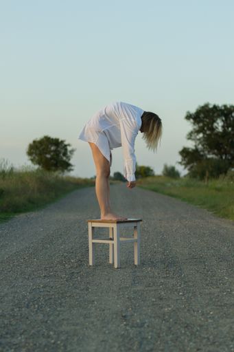 A vertical shot of a female in a white dress standing on a chair in the street
