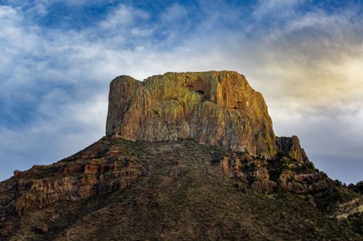 A scenic view of a rocky mountain in a rural area in cloudy sky background