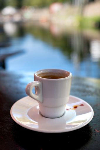 A close-up of a small cup of espresso on a blurred background of a lake