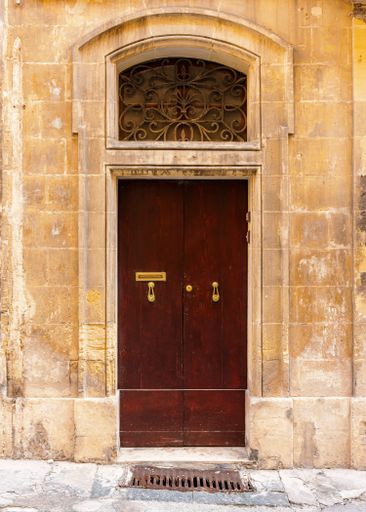 A vertical shot of a vintage brown front door of a yellow brick building in Valetta, Malta