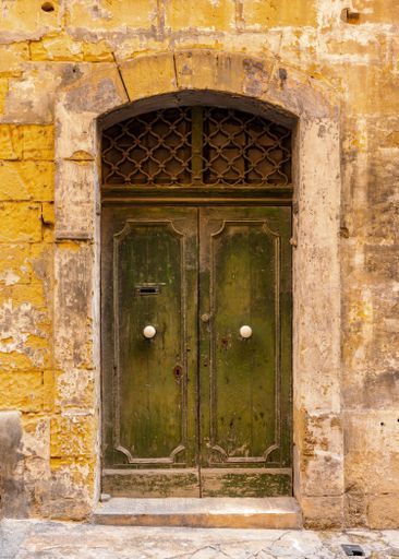 A vertical shot of a vintage green front door of a yellow brick building in Valetta, Malta