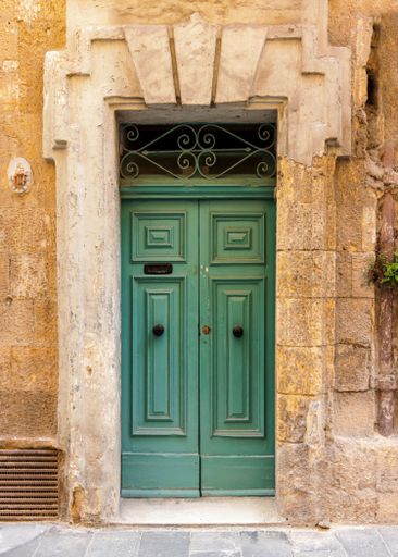 A vertical shot of a vintage green front door of a yellow brick building in Valetta, Malta