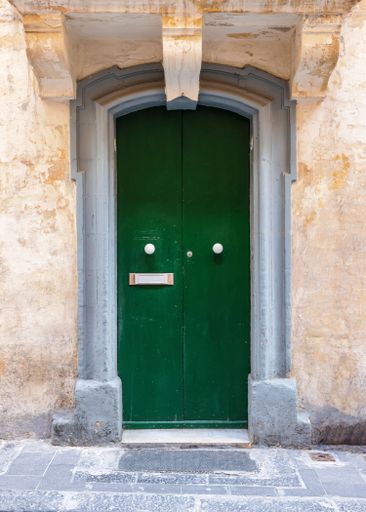 A vertical shot of a vintage green front door of an old beige building in Valetta, Malta