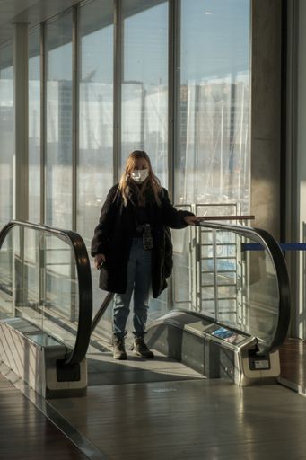 A vertical shot of a girl in a mask going up the escalator in Genoa, Italy