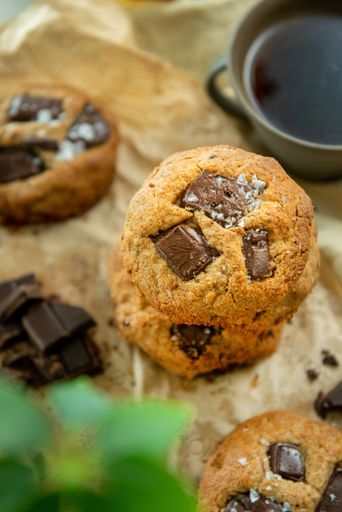 A vertical closeup of coffee cup and freshly baked cookies blurred background