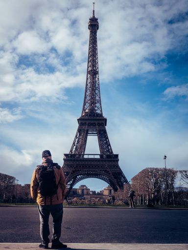 A vertical shot of the back of a tourist walking near the Eiffel Tower