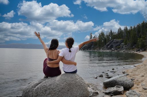 A back view of two young female friends sitting on a rock at the beach