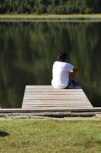 A vertical shot of a person sitting on a wooden pier on the lake coast