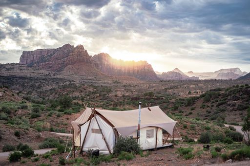 A white tent isolated in the field with rocky mountains on the background at sunrise