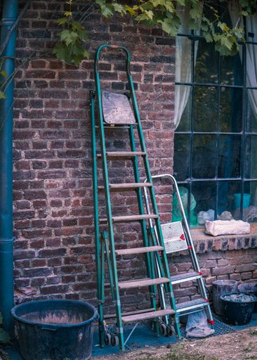 A vertical shot of big and small stepladders leaning on brickwall
