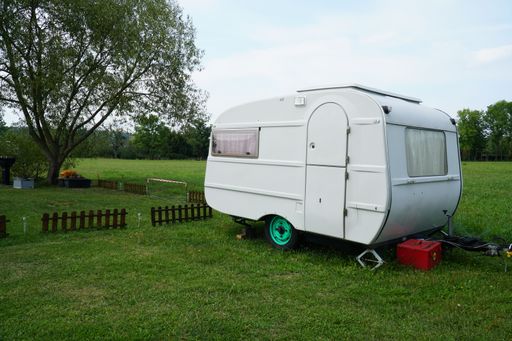 A small white travel trailer parked on a green field with a tree beside it