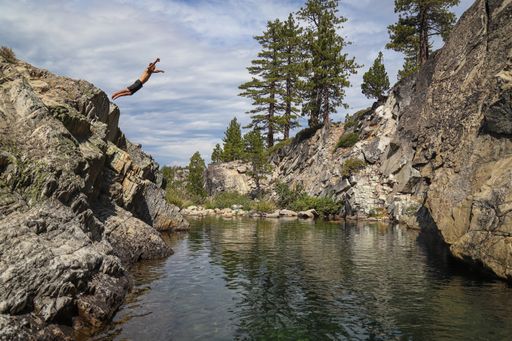 A daring man jumps from a stone cliff into a swimming hole deep in the Sierra Nevada backcountry.