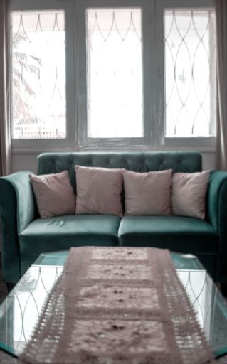 A vertical of a green sofa with white pillows in front of a glass table under the windows