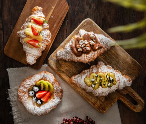 A top shot of gourmet croissants with powdered sugar and cream on a wooden board