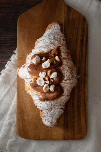 A vertical top view of a gourmet croissant with powdered sugar and chocolate cream on a wooden board