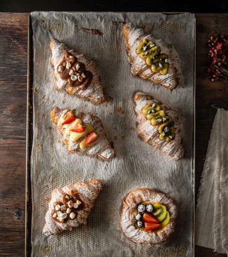 A vertical top view of gourmet croissants with powdered sugar and cream on a wooden board
