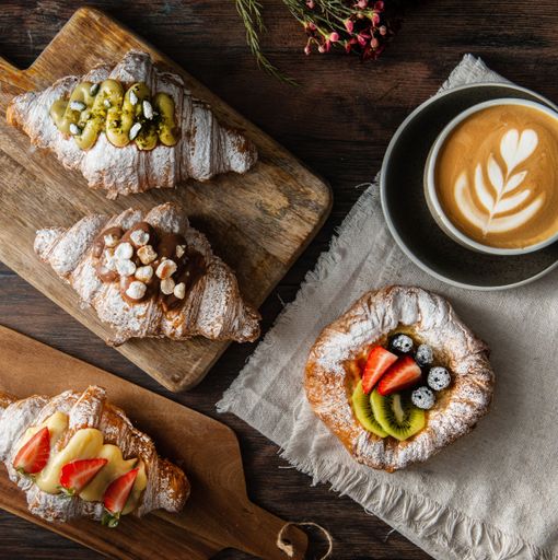 A top shot of gourmet croissants with powdered sugar, fruits and cream near a latte