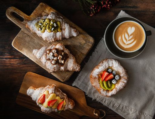 A top shot of gourmet croissants with powdered sugar and cream near a latte