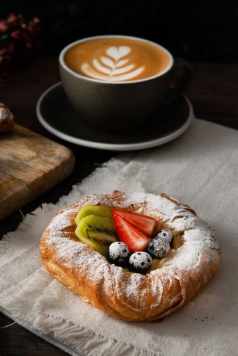 A vertical closeup shot of a pastry with powdered sugar and fruits near a latte