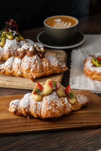 A vertical shot of gourmet croissants with powdered sugar and cream near a latte