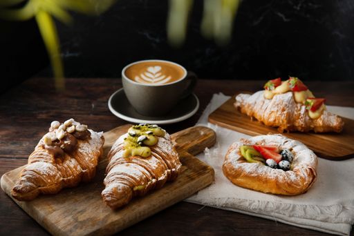 A closeup shot of gourmet croissants with powdered sugar and cream near a latte