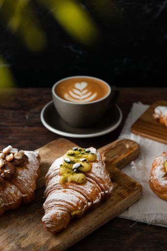 A vertical closeup shot of a gourmet croissant with pistachio cream near a latte