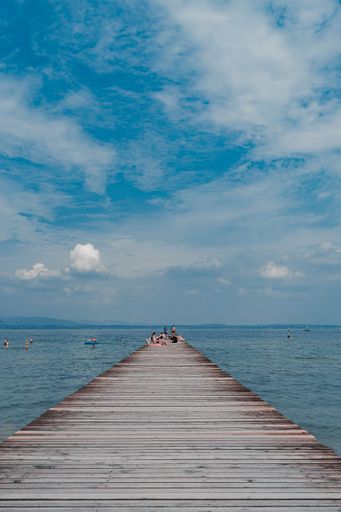 A scenic view of an outdoor beach with several people on a pier in Sirmione, Lake Garda, Italy