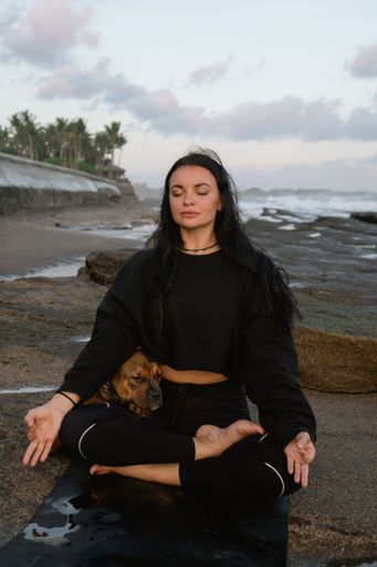 Breathing practice and pranayama. Yoga with a dog on the beach. Young woman doing relaxation and meditation session in Bali beach
