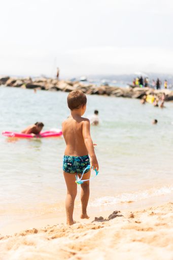 A vertical shot of a little boy on the sandy beach, shot from the back