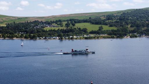 A drone view of a lake full of boats in the middle of hills with a clear sky in the background