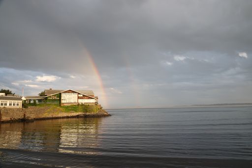 A scenic shot of two rainbows in the grey cloudy sky over a calm sea in Swampscott, Massachusetts