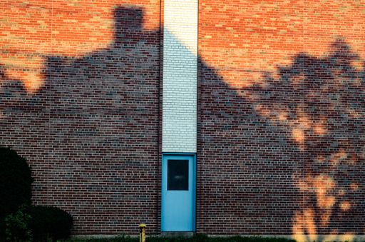 A beautiful shot of a brick wall with a blue door covered by shadows of house and trees