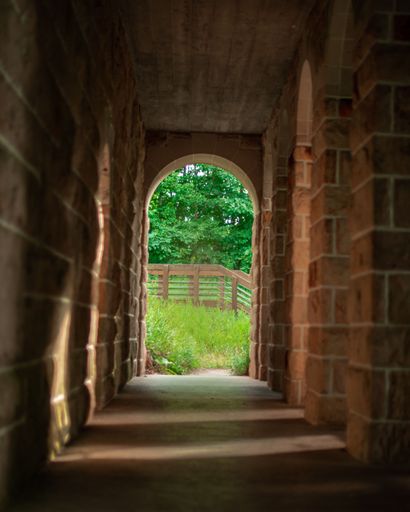 A vertical shot of a building with stone arch a green park in the background