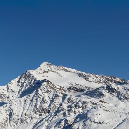 A closeup shot of a rocky peak covered with snow under the bright blue sky