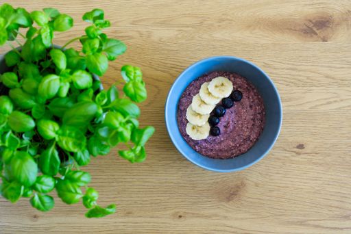 A top view of a blueberry smoothie bowl decorated with berries and sliced bananas near a basil herb