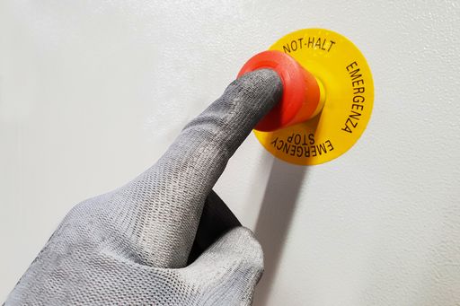 A closeup shot of male hand with gloves on red emergency stop button