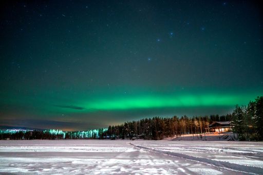 A panoramic view of the Aurora Borealis over a frozen lake in Lapland, Finland