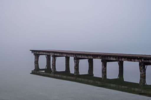 Wooden walkway juts out into a lake and a thick fog hangs over the water