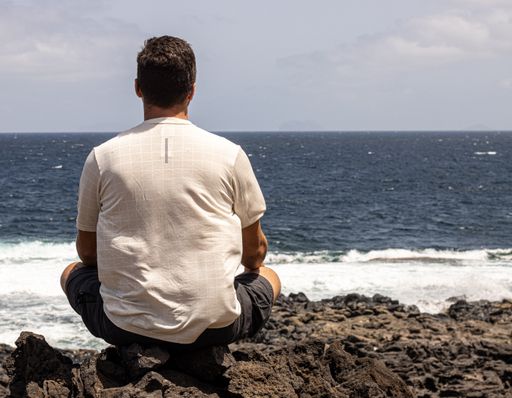 A selective focus shot of a Caucasian male sitting near the sea and relaxing