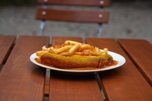 A closeup shot of sausage with mustard sauce and french fries on a wooden table
