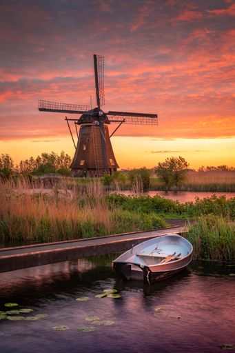 A vertical shot of a small boat in a lake and a mill in the background under the cloudy sunset sky
