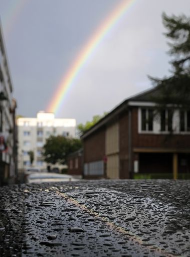 A vertical closeup shot of raindrops on a street with a rainbow in the background