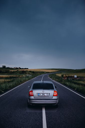 A vertical shot of a car standing on a long asphalt road on a rainy day in the countryside