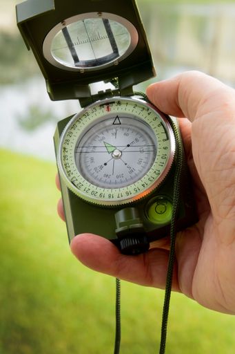A closeup of a caucasian person holding a green navigation compass in their hand