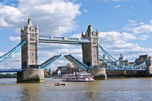 A boat sailing under the tower bridge in London with a cloudy sky in the background