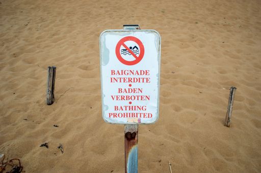 A closeup shot of a rusty sign planted in the sand and telling that swimming is prohibited